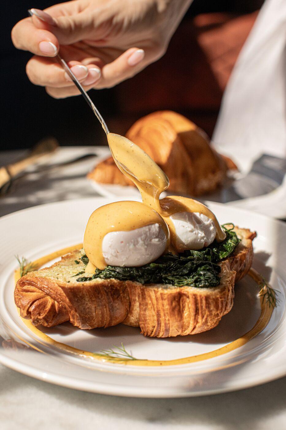 Hollandaise poured over croissant eggs Benedict